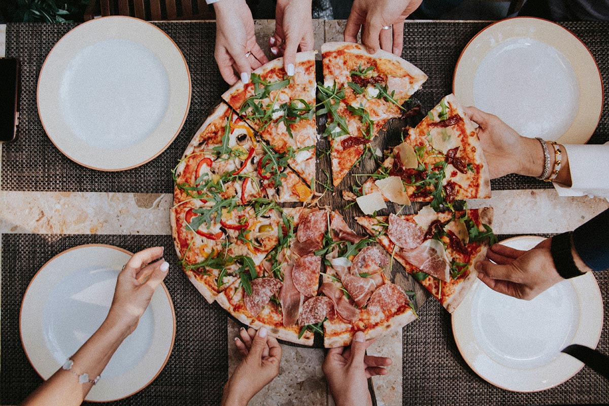 Une pizza garnie de produits Herta. L'ambiance est chaleureuse avec une lumière douce et des expressions joyeuses.